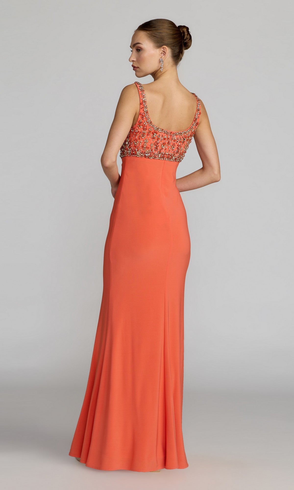 A woman stands with her back to the camera against a plain background, wearing the Mac Duggal 2253 long formal dress, which features a sleeveless design, floor-length coral skirt, and a crystal-embellished bodice.